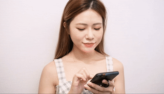 一位身穿格子連身裙的女士站在純白色的背景下，正在看著她的智慧型手機。.