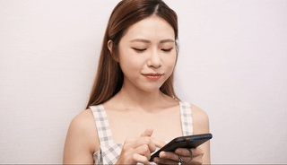 一位留著長髮、穿著格子上衣的女士站在樸素的背景下看著手機。.