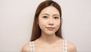 留著棕色長髮、穿著格子無袖上衣的女人在純白色的背景下輕輕微笑。.